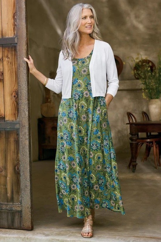 Green floral maxi dress with a white cardigan in a doorway, layered summer look for women over 60