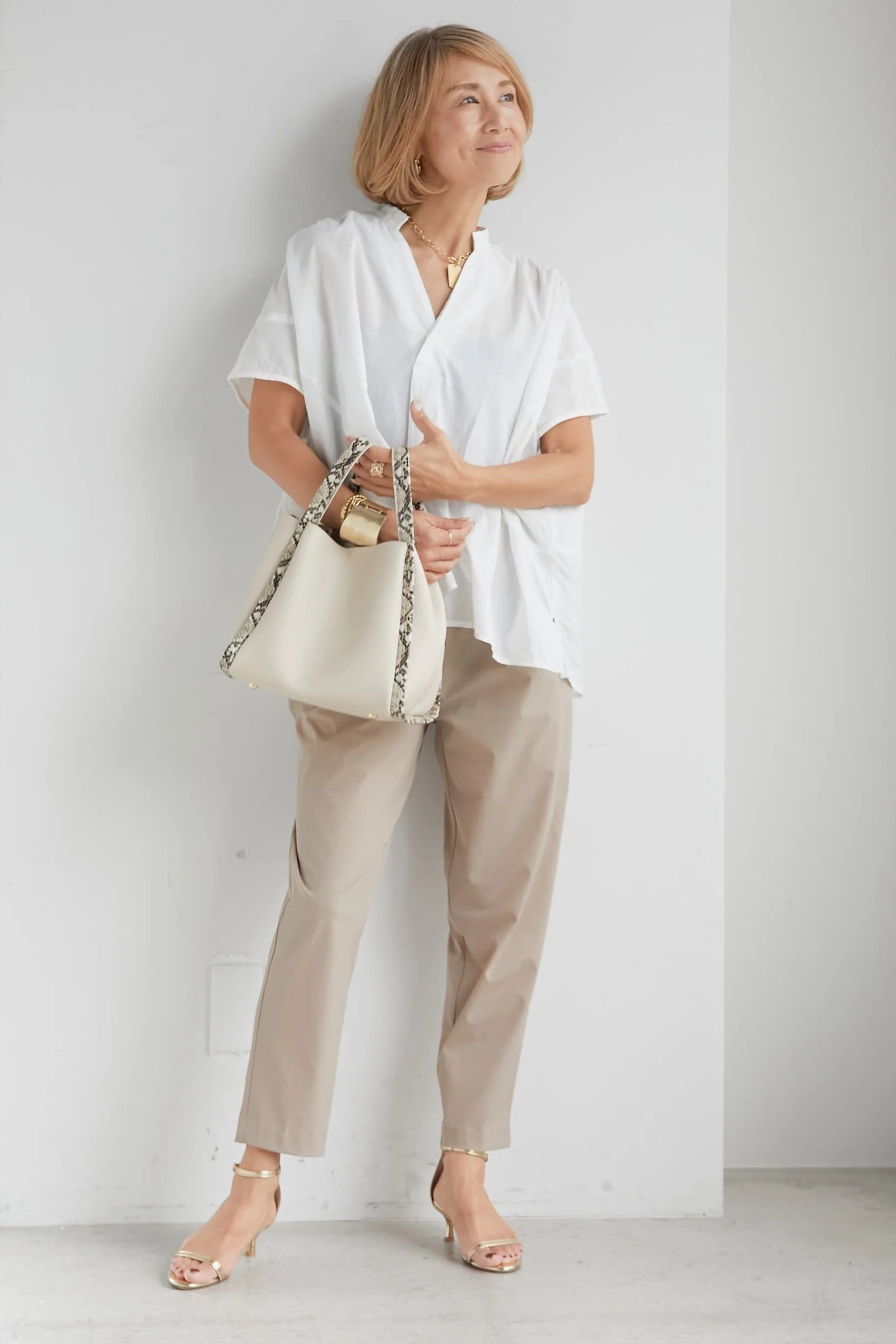 White button shirt with beige trousers in a studio, minimalist fall outfit for mature women