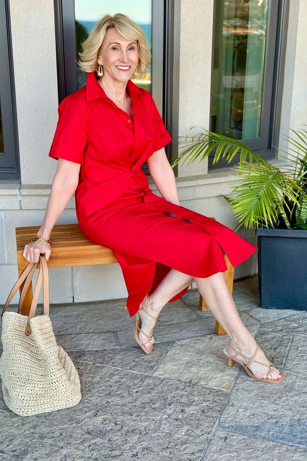 Red sleeveless midi dress with a straw tote, seated summer look for mature women