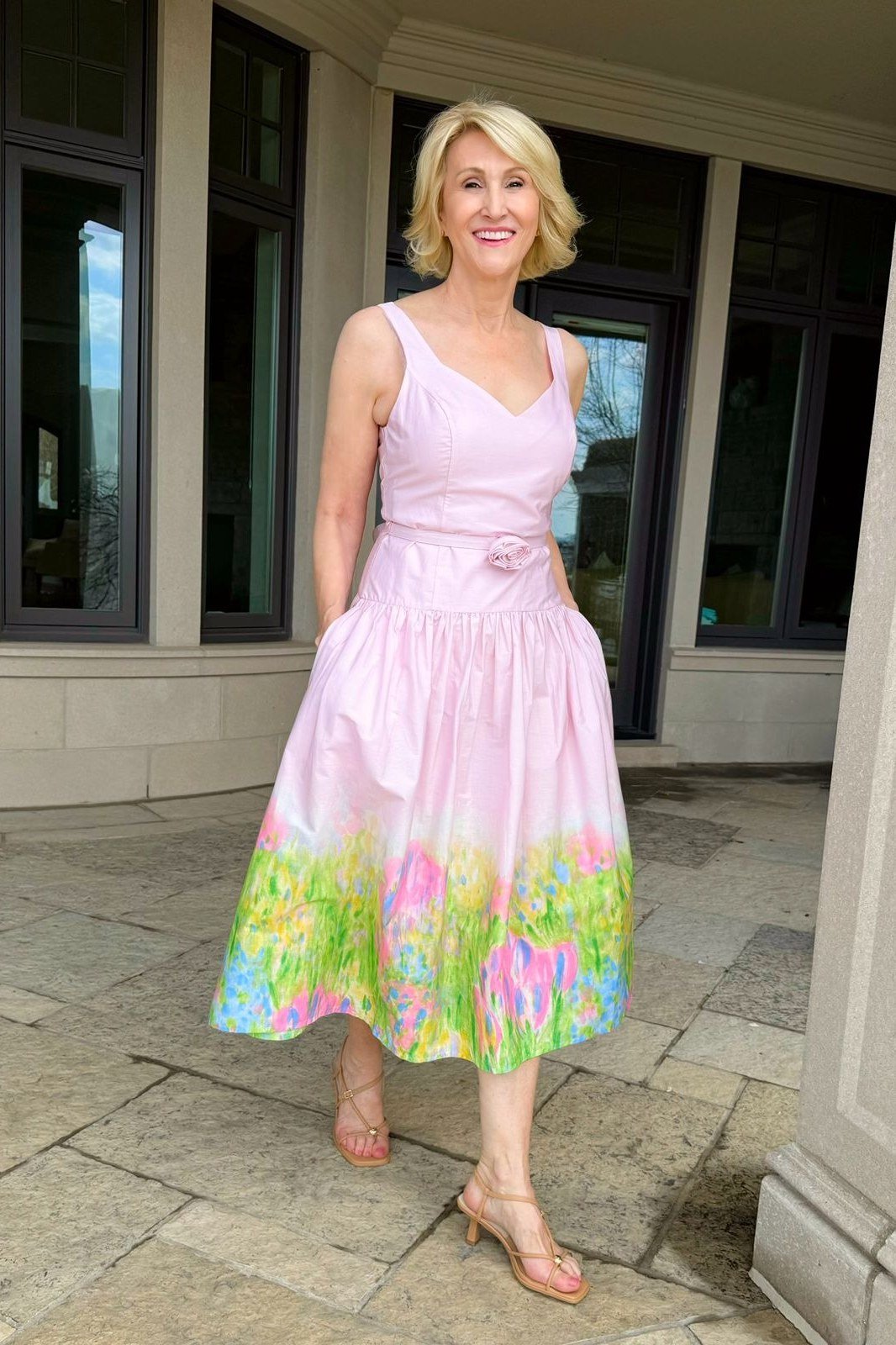 Pink floral sleeveless midi dress on blonde older woman, stone patio