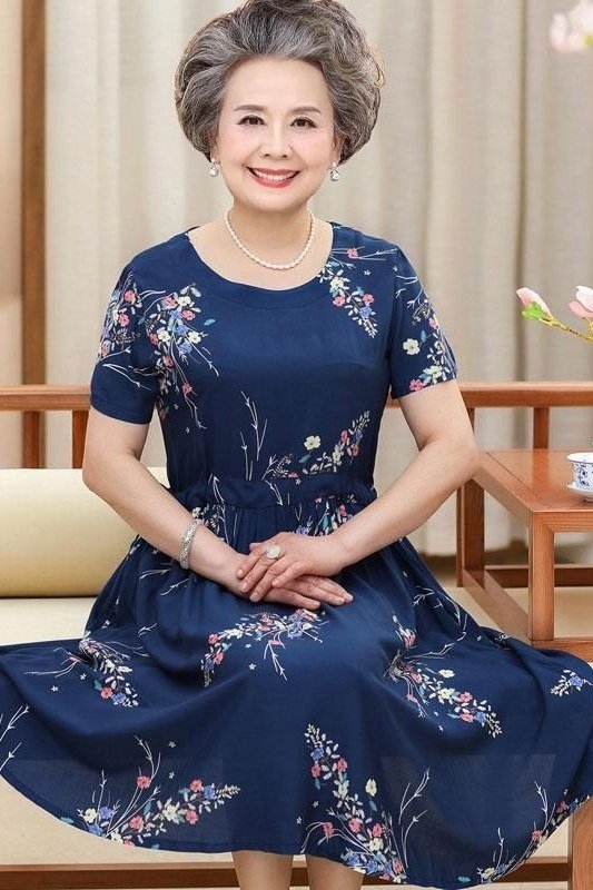 Navy dress with tiny white floral print, pearl necklace, seated
