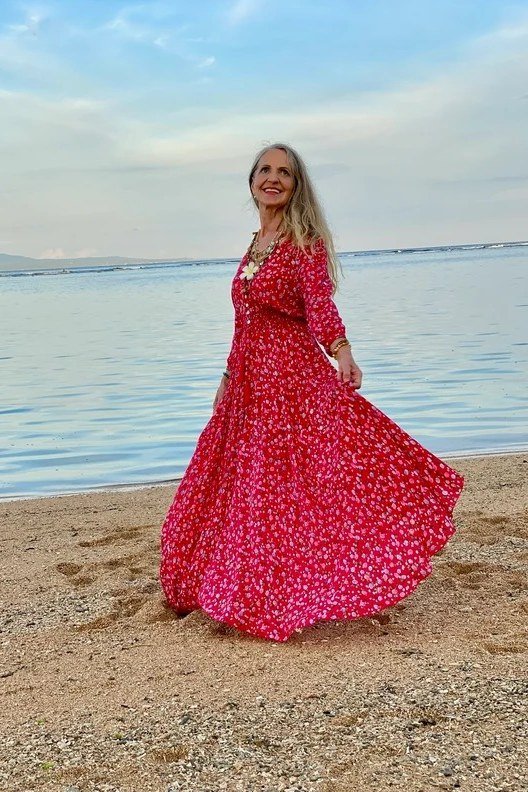 Red and pink floral maxi dress twirling on beach, older woman
