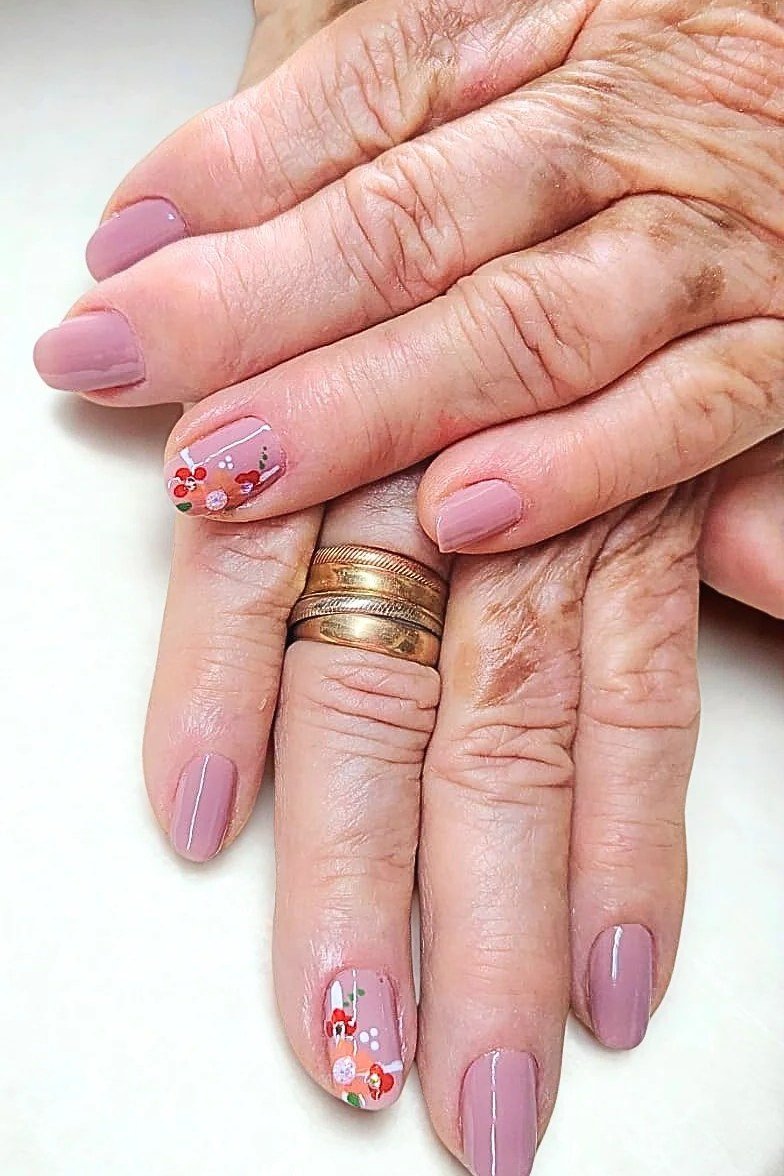 Pink and red floral nail art on mature hands for women over 50