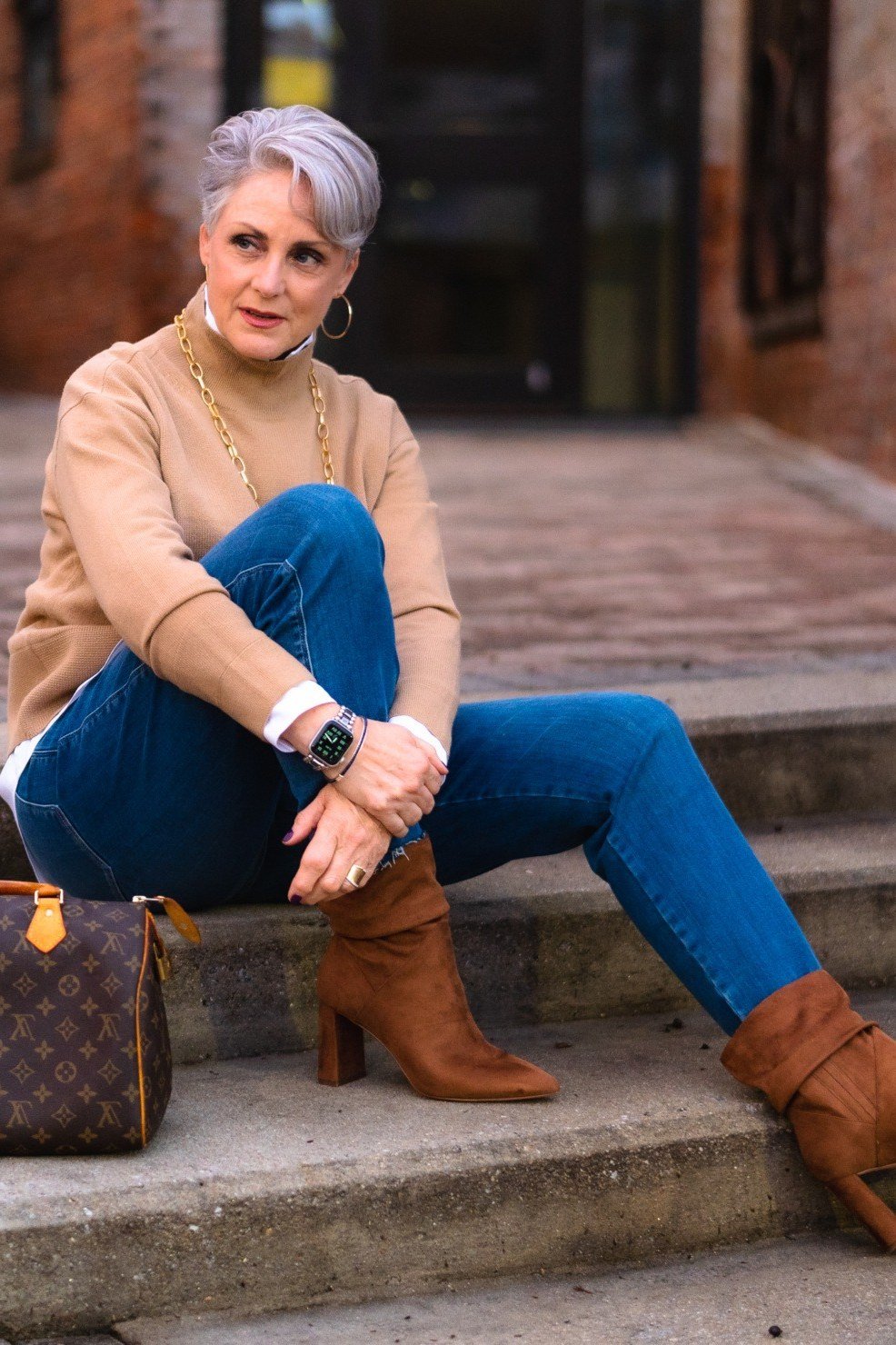 Tan turtleneck sweater, bright blue jeans, tan heeled boots, woman on city steps