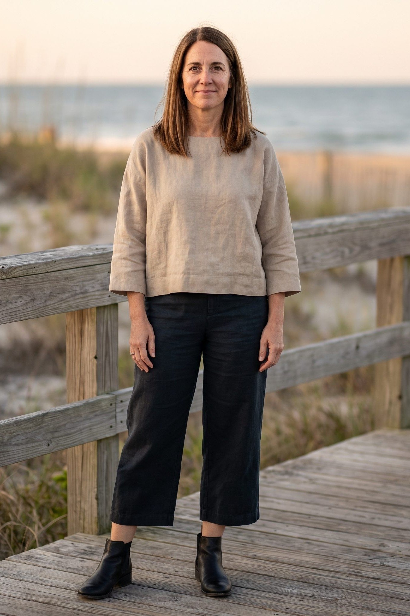 Beige knit sweater, black wide-leg pants, black ankle boots, woman on boardwalk