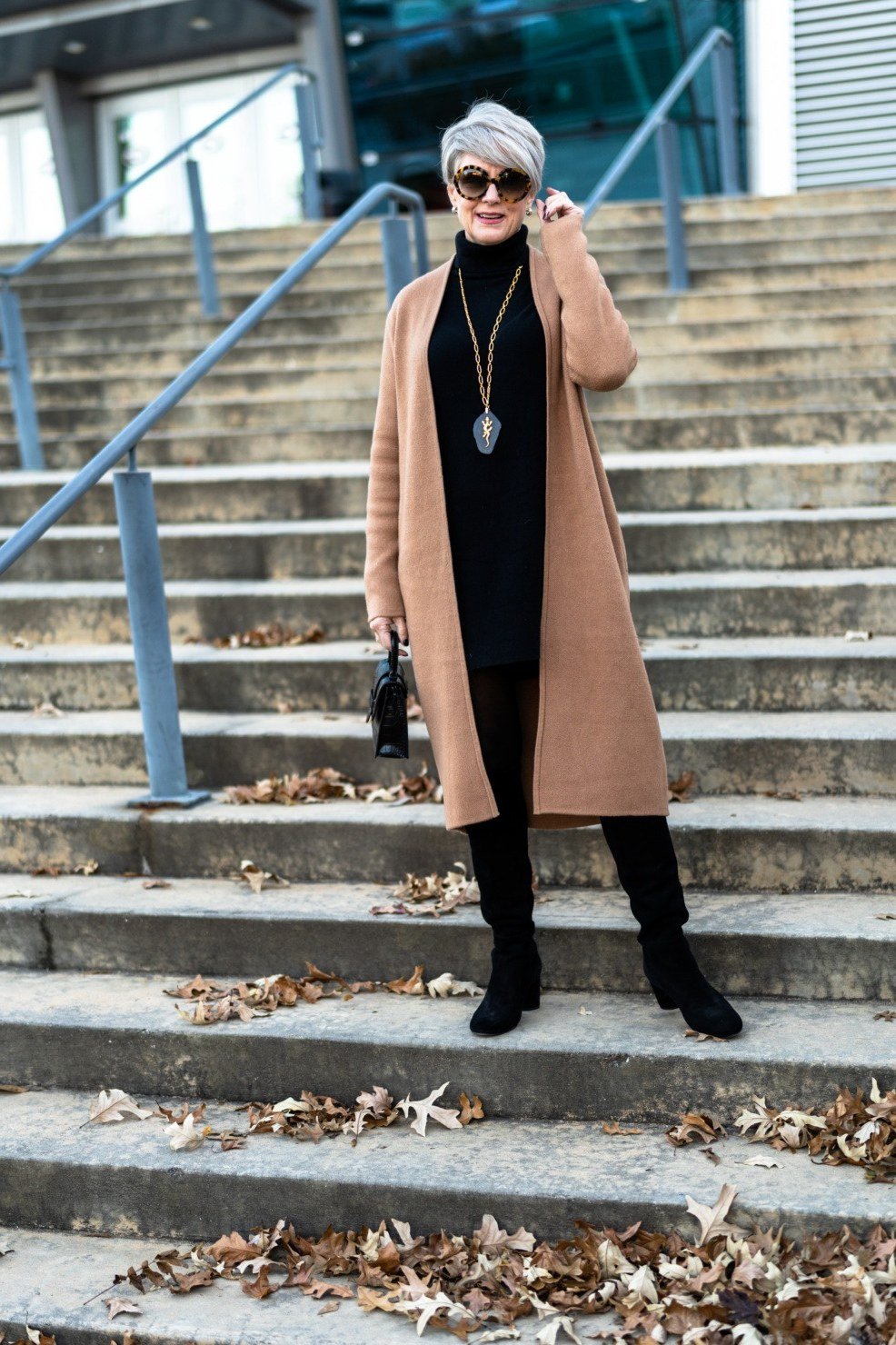 Camel coat, black turtleneck and slim pants, black boots, woman on steps