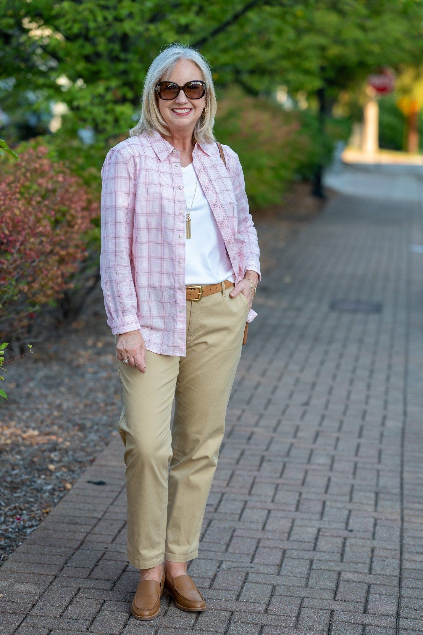 Pink plaid shirt, khaki pants, tan loafers, woman on brick path