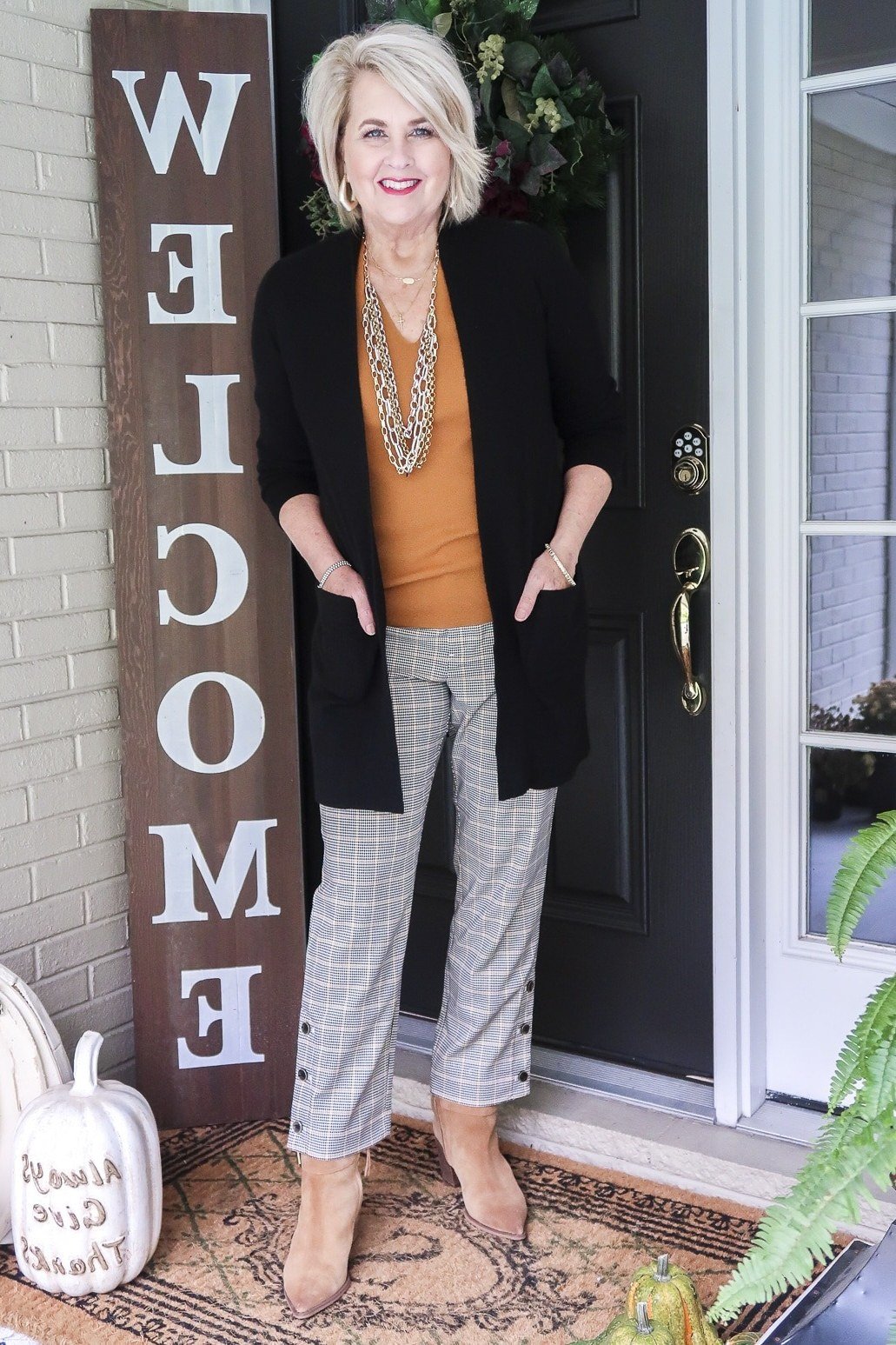 Long black cardigan, mustard yellow top, gray plaid pants, woman on porch