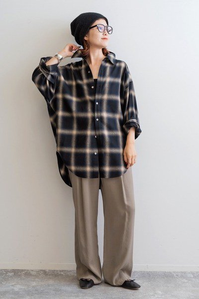 Oversized dark plaid shirt, taupe wide-leg pants, black beanie, woman at wall
