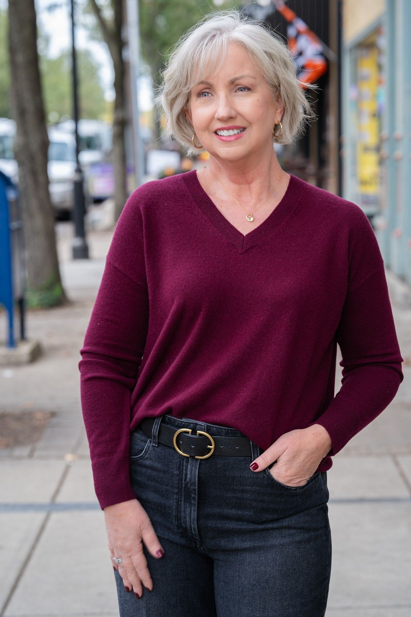 Burgundy v-neck sweater, dark jeans, statement belt, woman on sidewalk