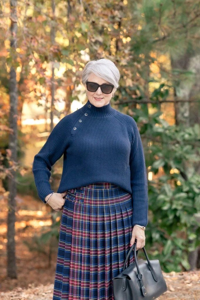 Navy turtleneck sweater, red navy plaid pleated midi skirt, woman in woods