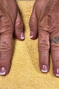 Elderly dark-skinned hands with white french tips on a yellow towel