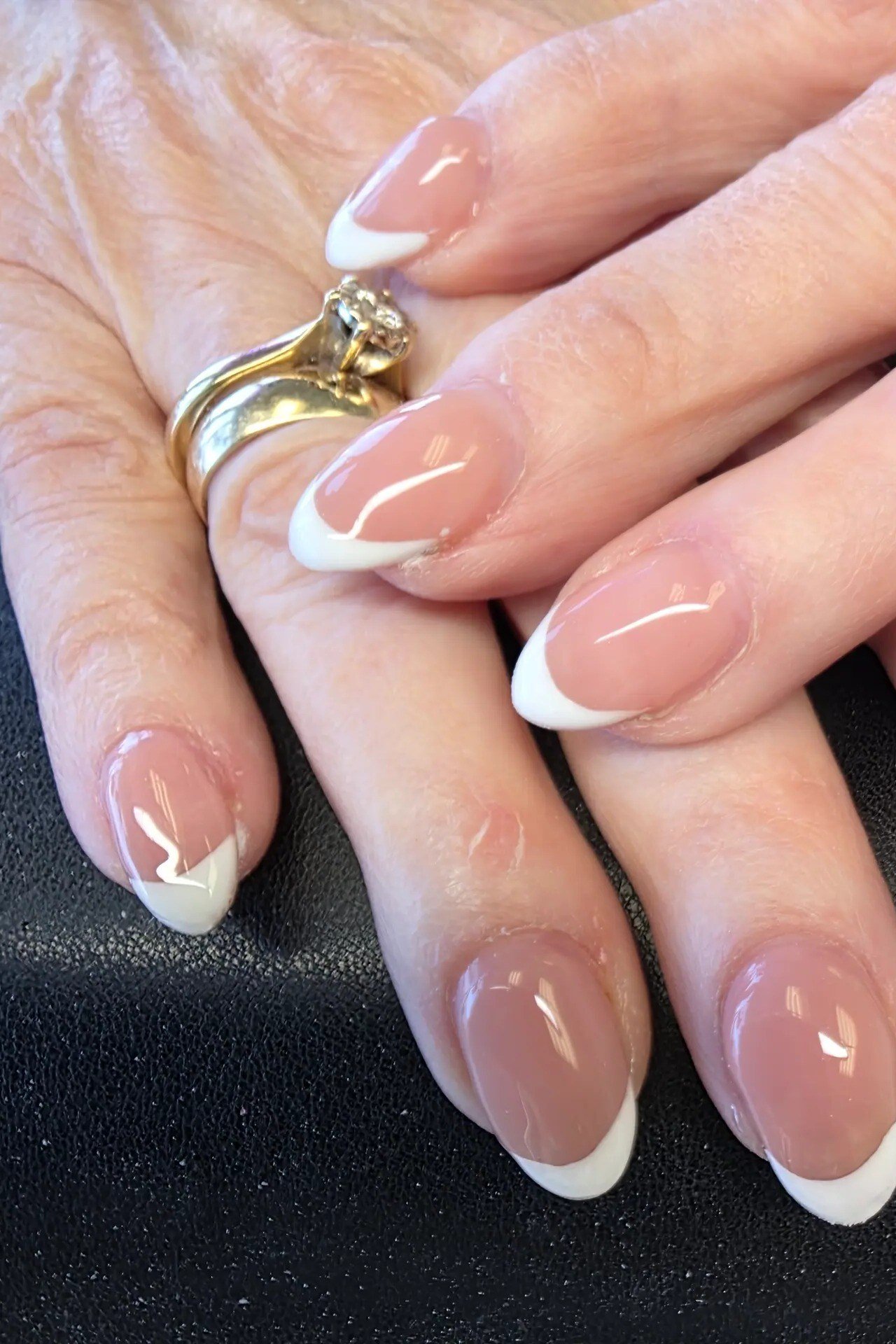 Pale pink french manicure with gold rings on an older hand