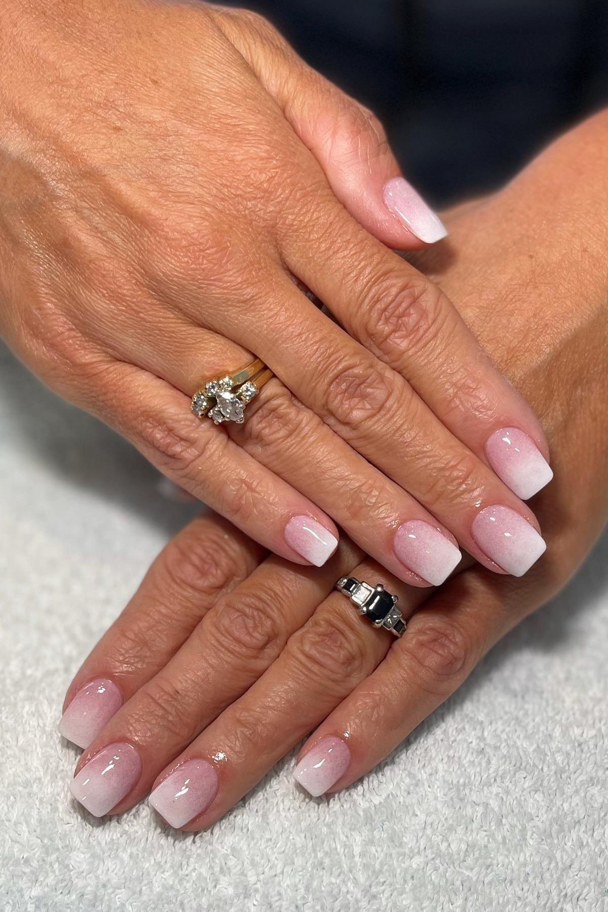 Pink and white french manicure on older hands with rings