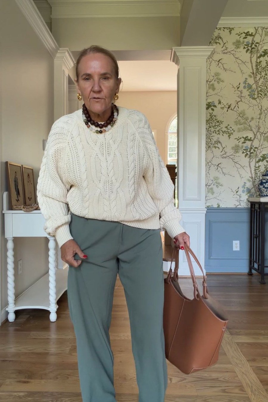 Fall sweater outfit idea 2 for women over 60: cream cable-knit sweater with sage pants