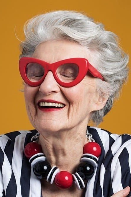 Short white pixie haircut on laughing older woman wearing bold red glasses