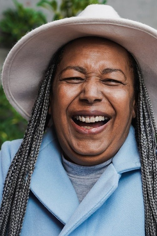 Long silver box braids with white hat on laughing older Black woman
