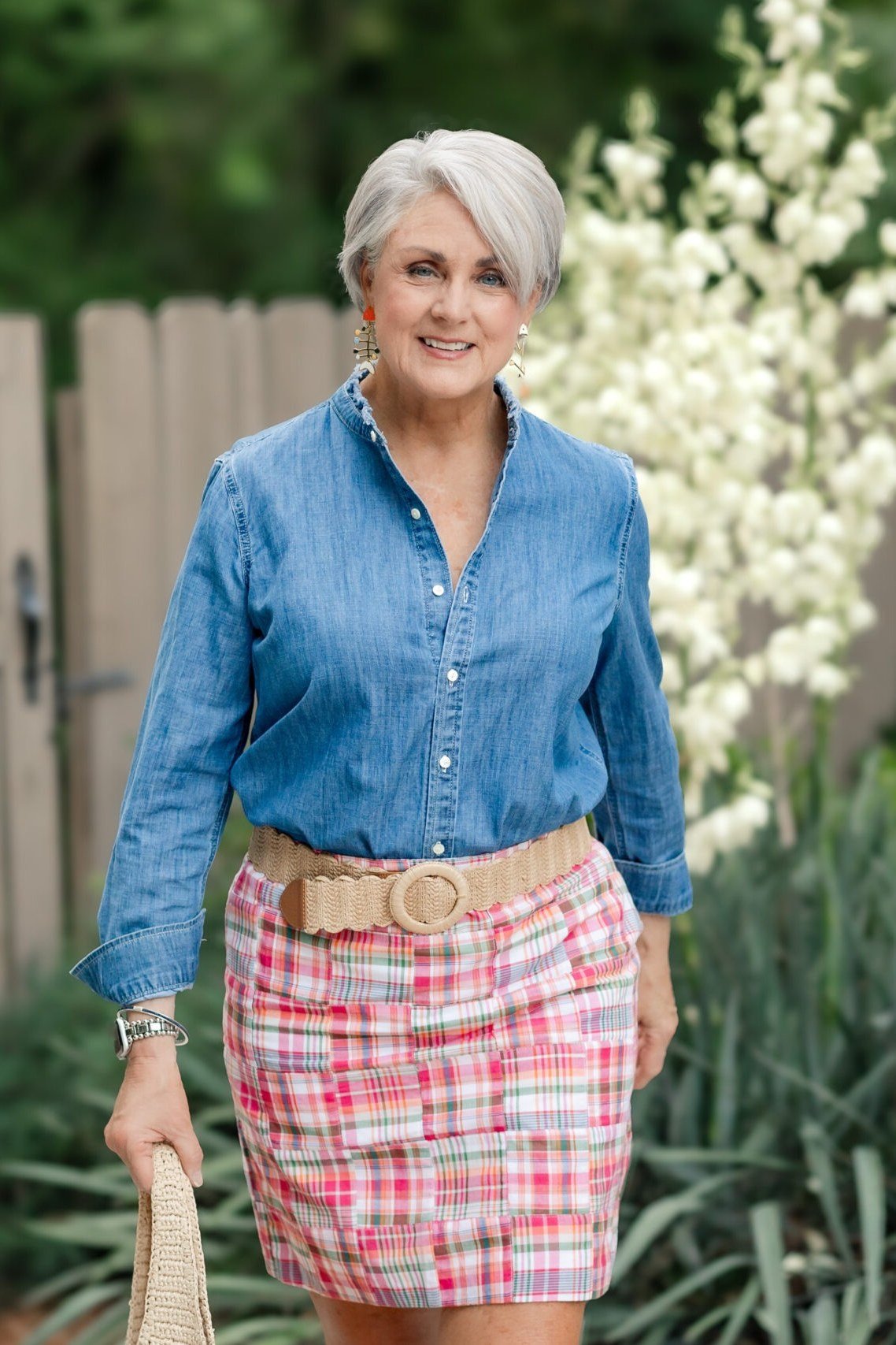 Woman over 70 in chambray shirt and pink plaid skirt in a garden
