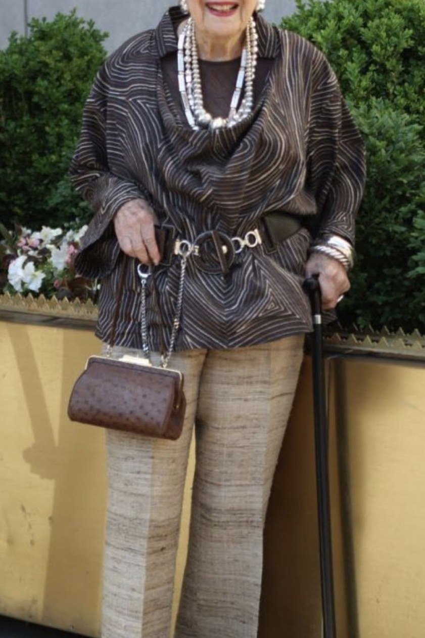 Older woman in patterned top and metallic wide pants with a cane