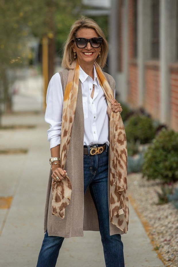 Senior woman in white shirt, tan vest, jeans and leopard scarf