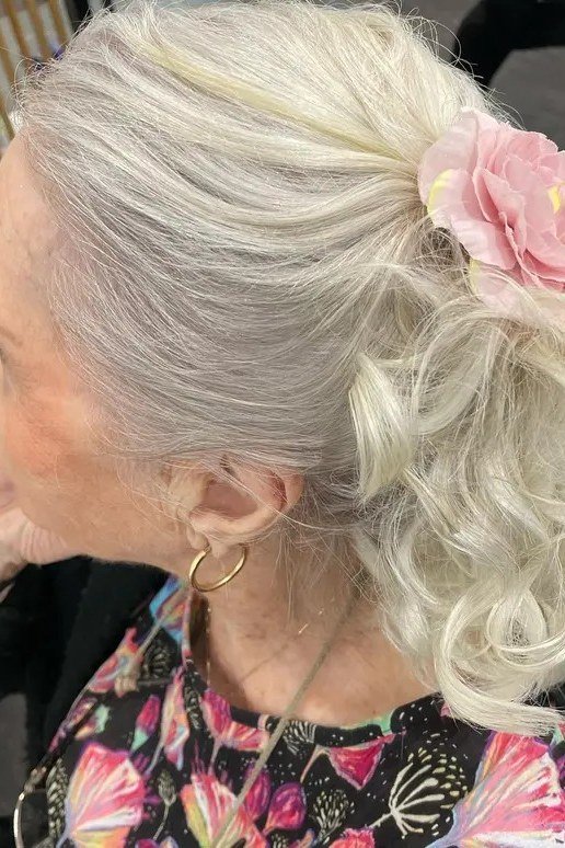 White Curly Updo With Pink Floral Hair Accessory - Christmas party hairstyle for women over 60 (white curly updo with pink floral hair accessory, side view)
