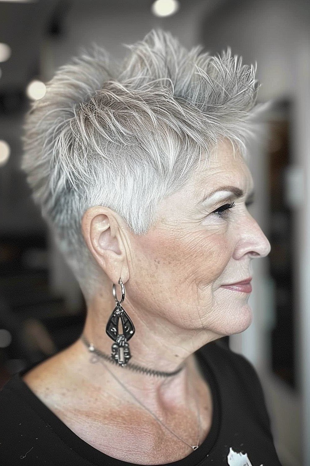 Grey pixie haircut for women over 50: silver pixie, side profile, long black earrings