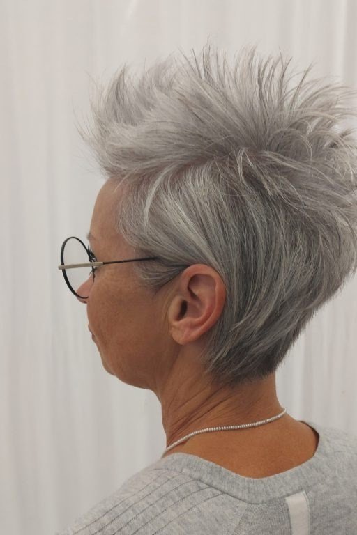 Grey pixie haircut for women over 50: silver pixie, side-back view with glasses