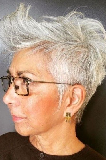 Grey pixie haircut for women over 50: white pixie with glasses, three-quarter view, dark background