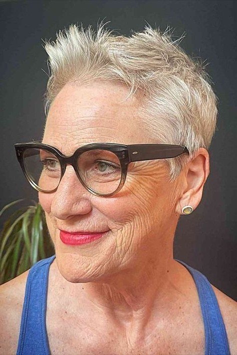 Grey pixie haircut for women over 50: silver pixie with black glasses, front view, smiling, blue top
