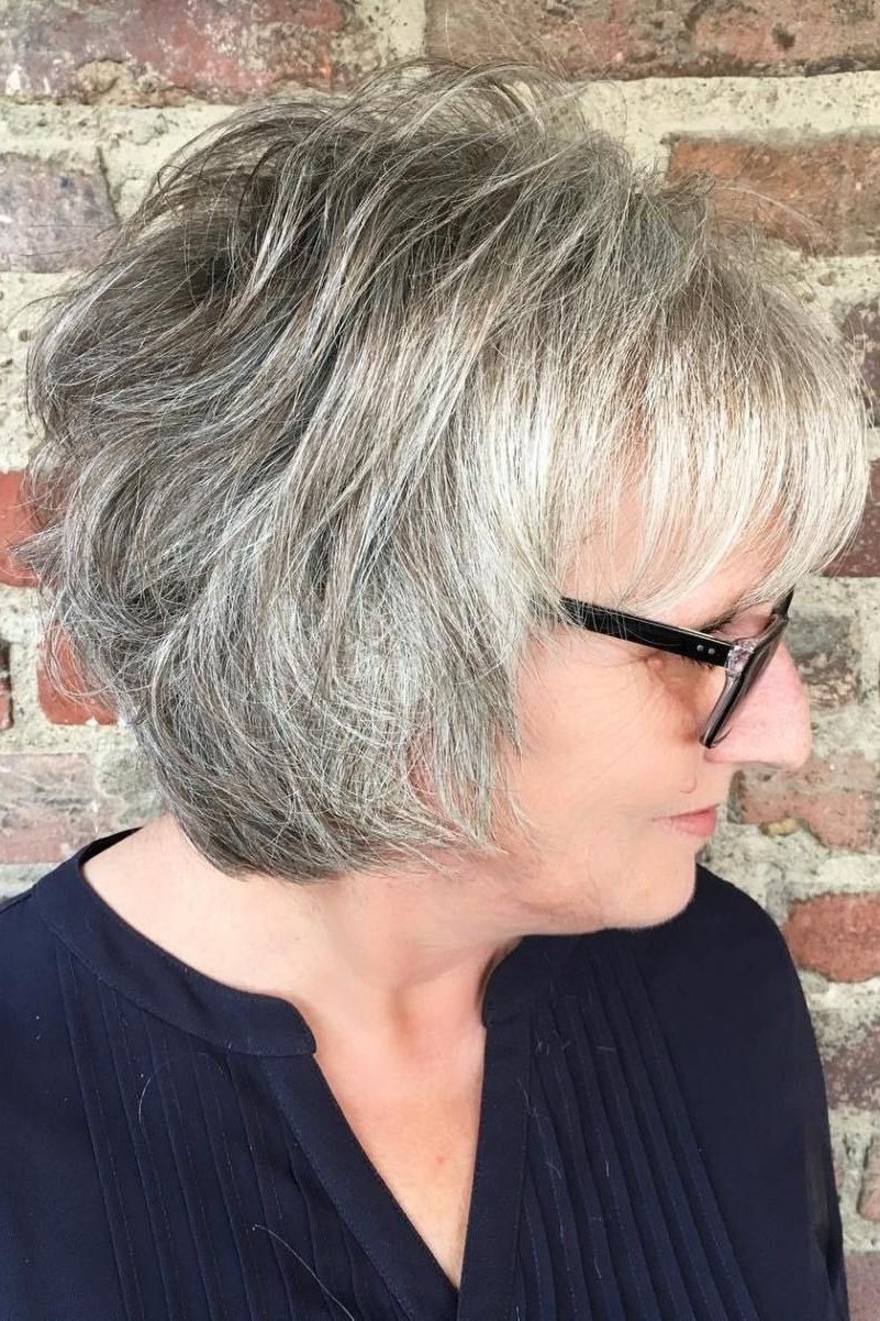 Grey pixie haircut for women over 50: silver shaggy pixie, side view, brick wall
