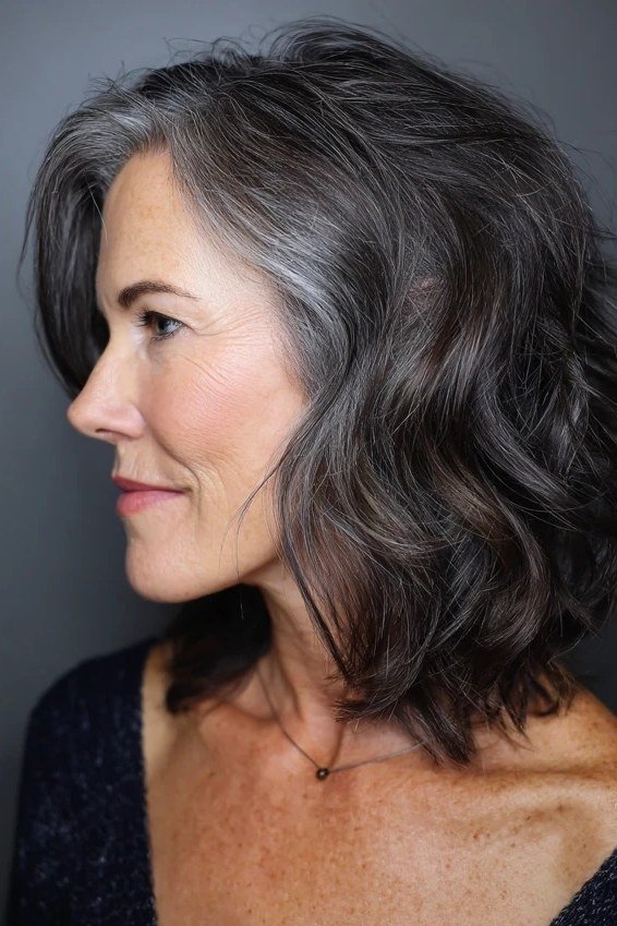 Wavy layered bob hairstyle for women over 50: dark grey wavy bob, side profile, steel tones