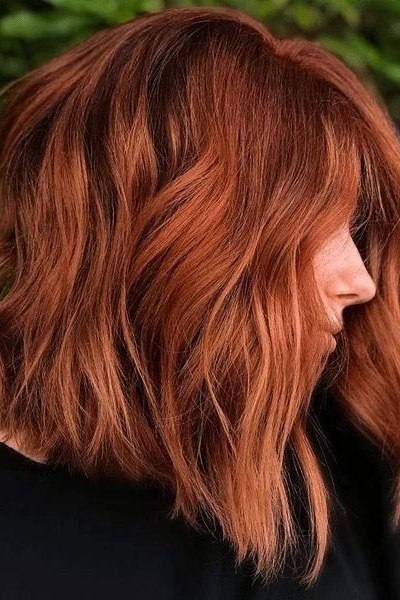 Wavy layered bob hairstyle for women over 50: copper wavy bob, side view, outdoor, sunlit