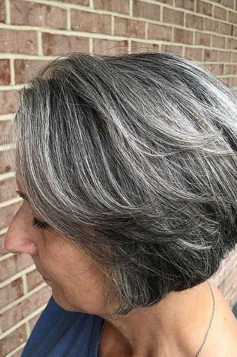 Salt-and-pepper bob haircut against brick wall, side view