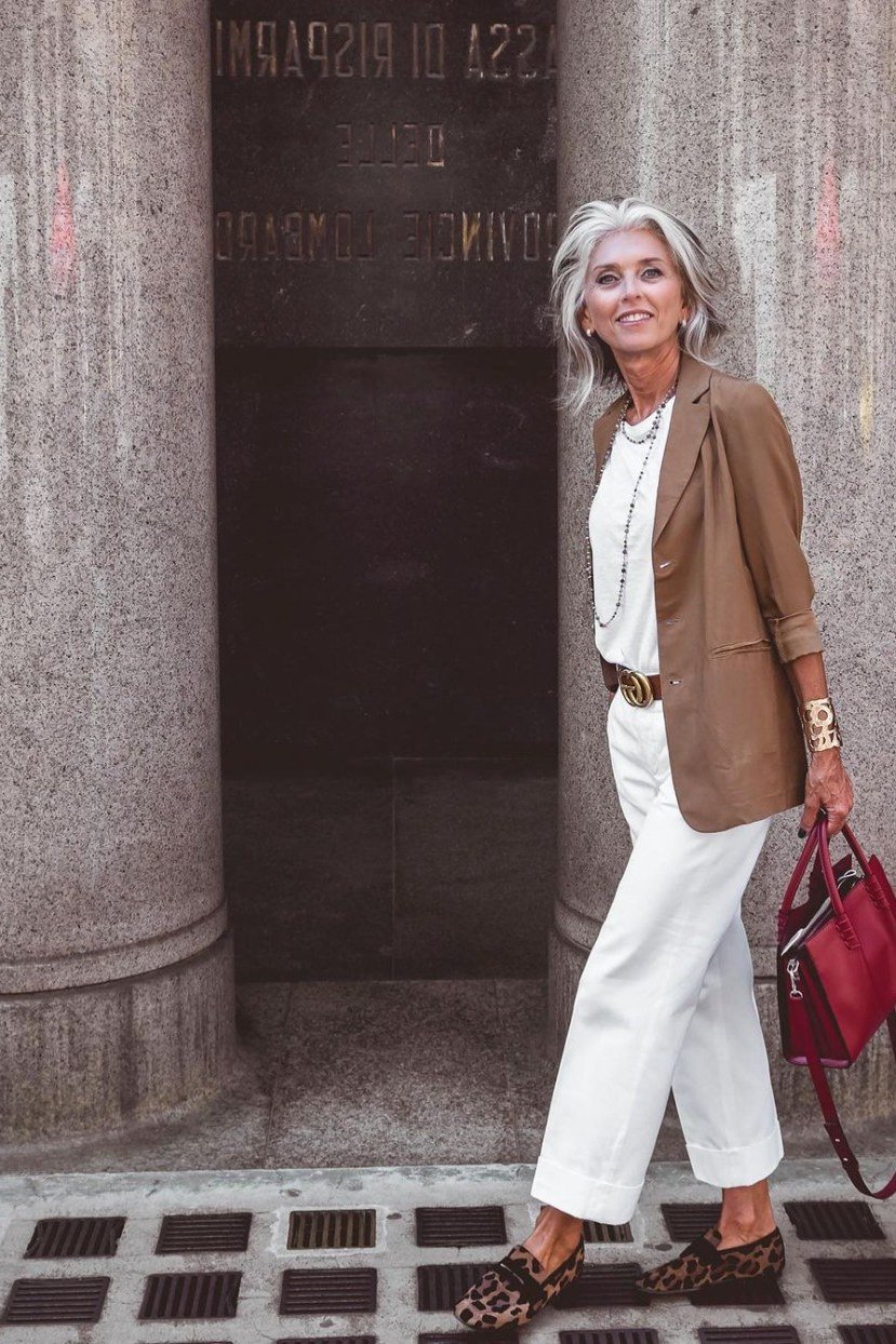 Woman over 50 wearing a brown blazer with white wide-leg trousers and red handbag, Italian street style