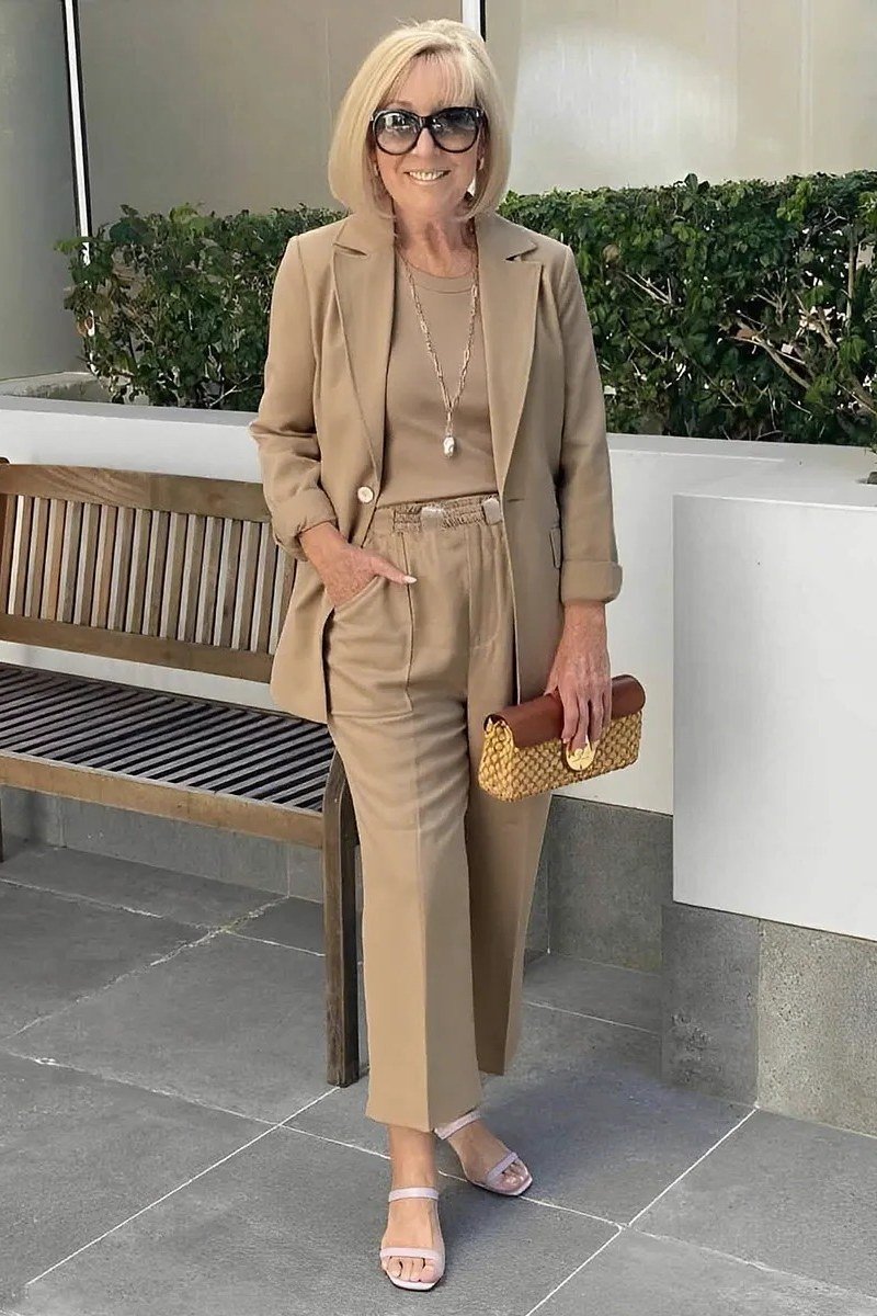 Woman over 50 in a taupe monochrome blazer suit with woven clutch, Italian style