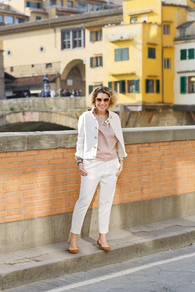 Woman over 50 wearing a white blazer with blush pink top and white trousers