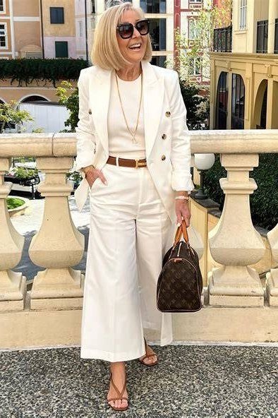 Woman over 50 in a cream blazer with brown belt and wide-leg trousers