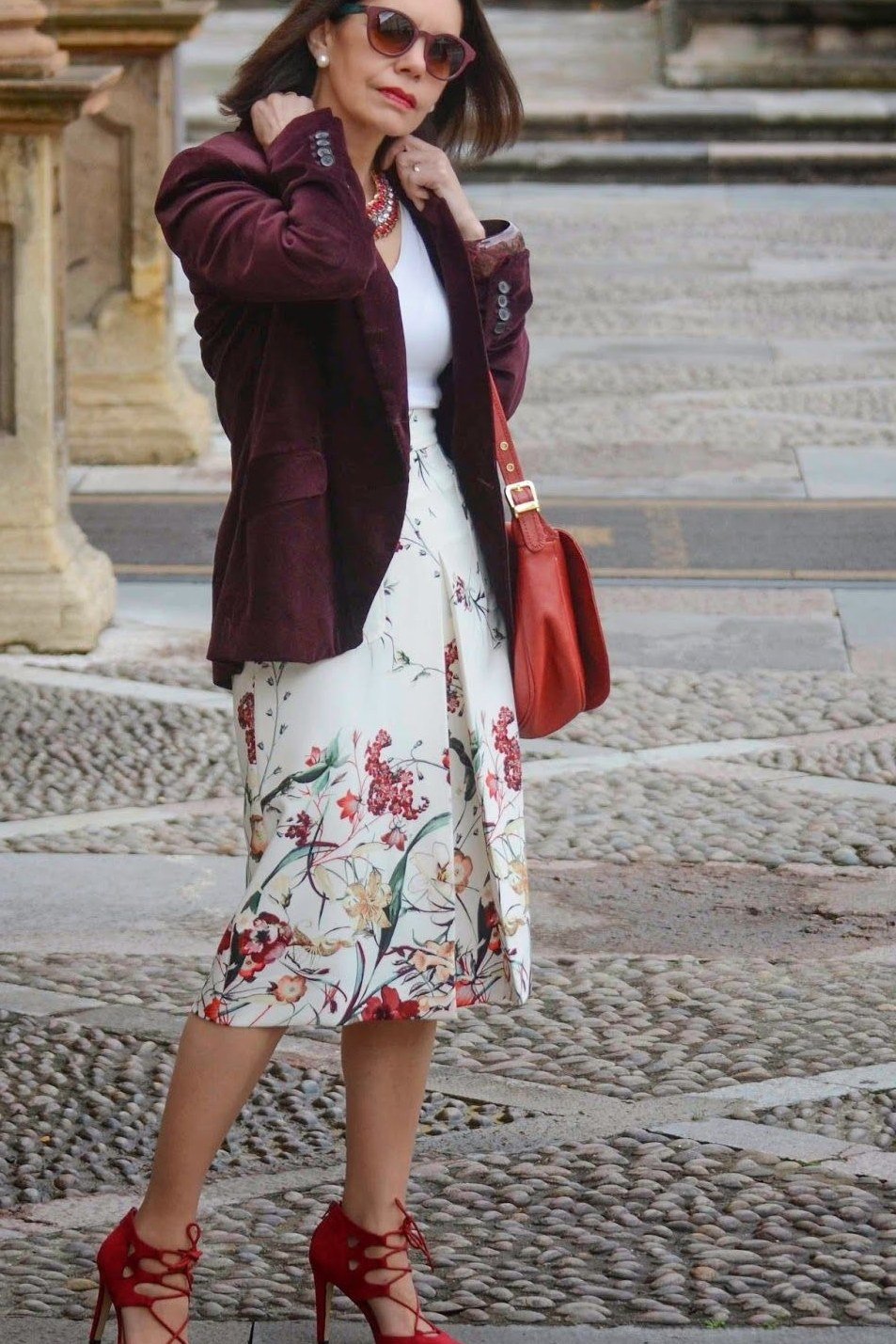 Woman over 50 wearing a burgundy blazer with floral midi skirt and red heels
