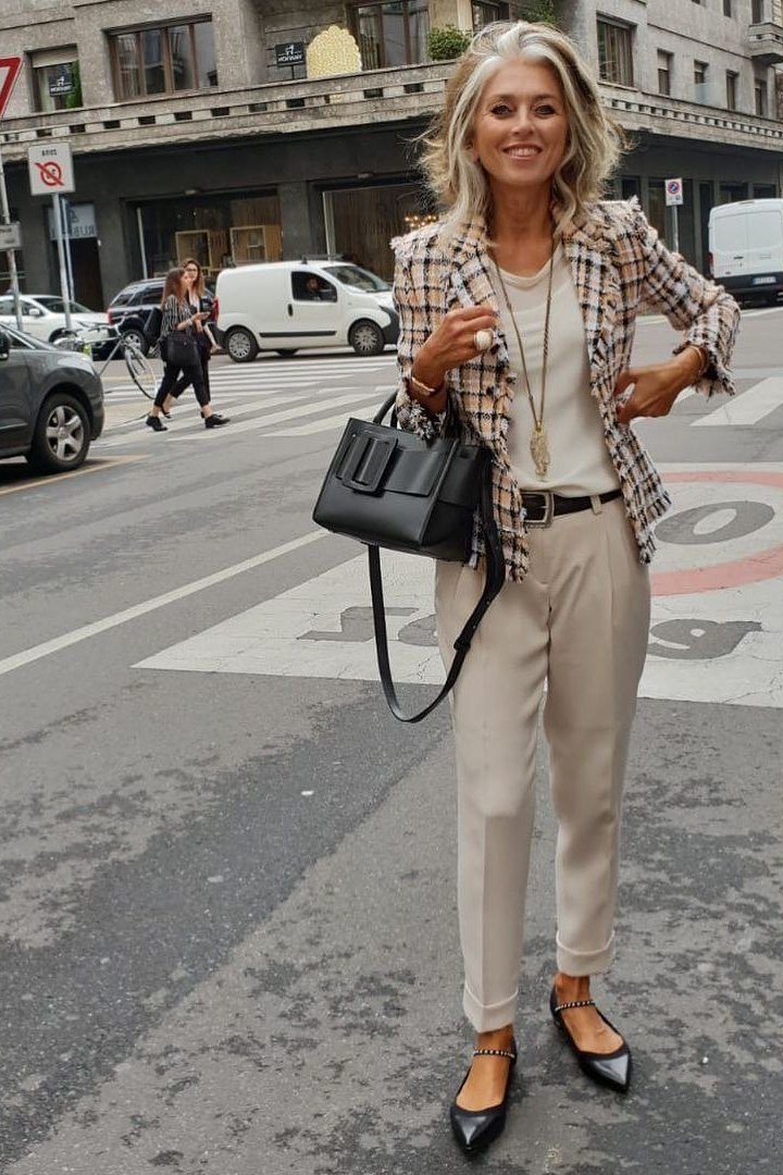 Woman over 50 in a plaid blazer with beige trousers and black handbag