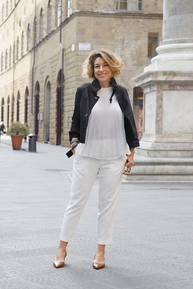 Woman over 50 wearing a black blazer with white jeans and nude heels