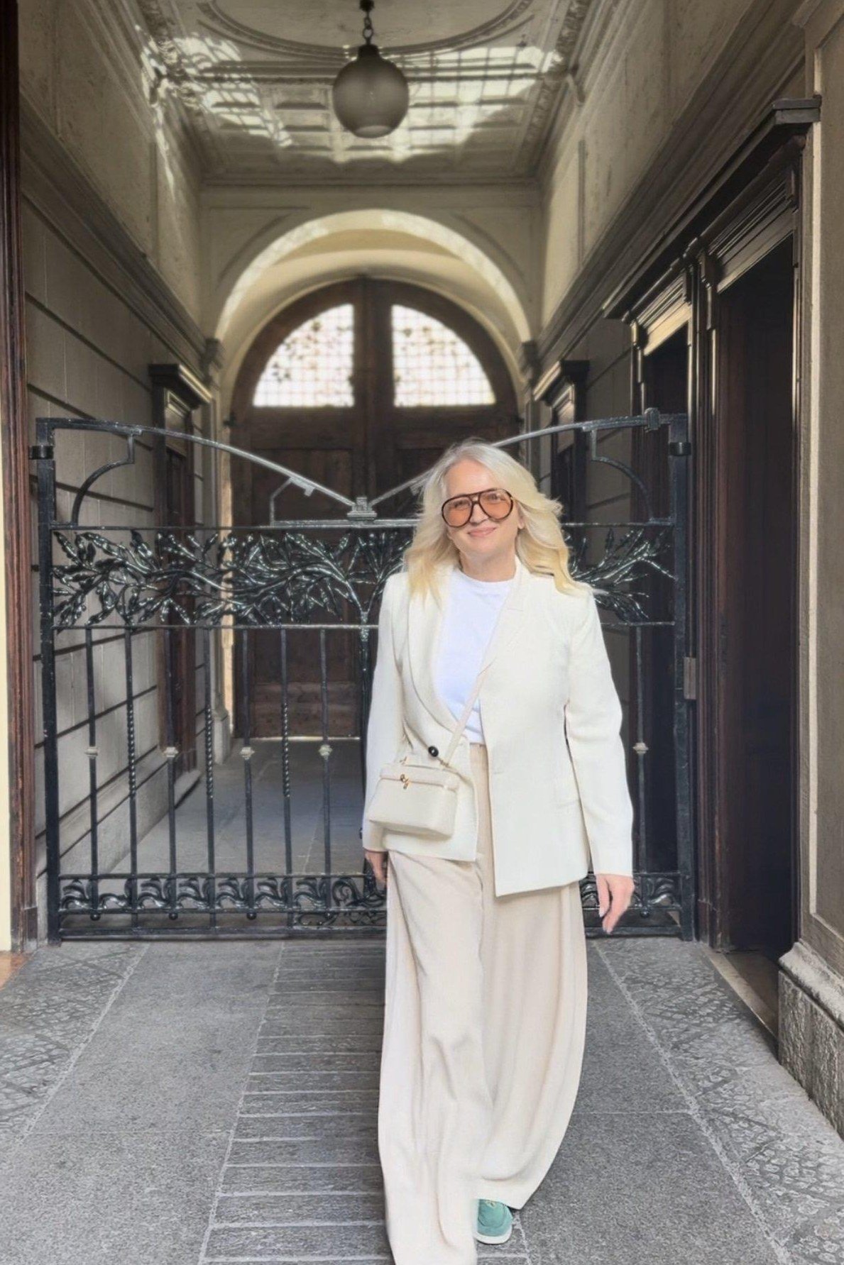 Woman over 50 in a softly tailored white suit walking through a grand corridor