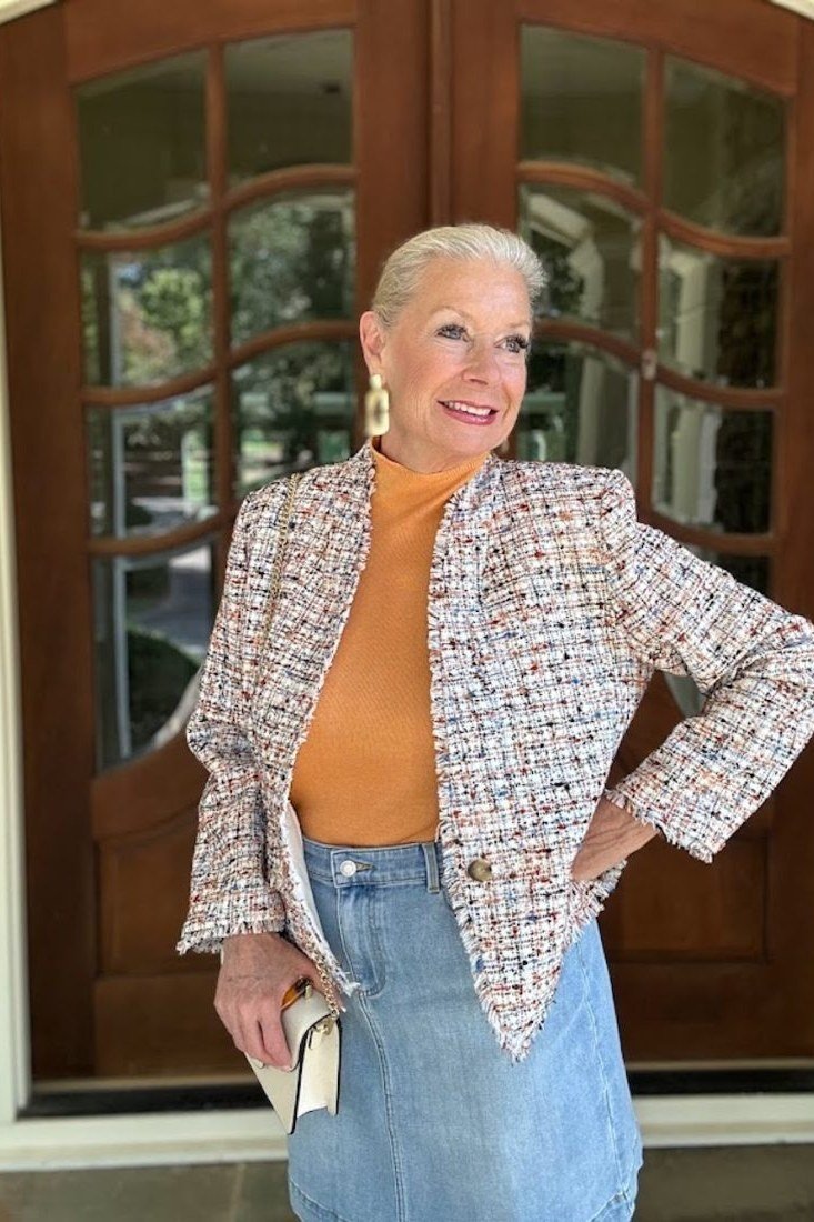 Woman over 50 in a tweed jacket with orange top and denim midi skirt