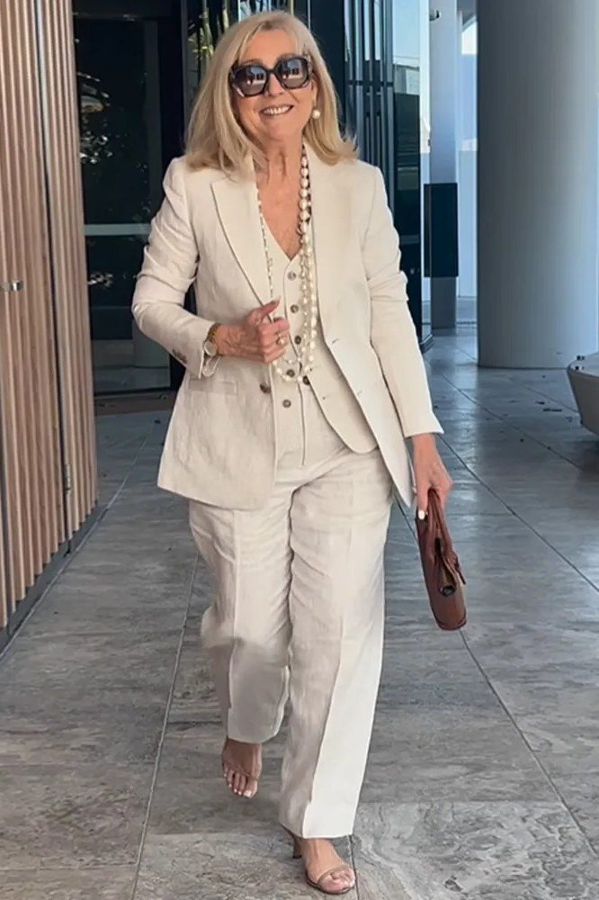 Woman over 50 wearing a cream blazer suit with layered pearl necklaces