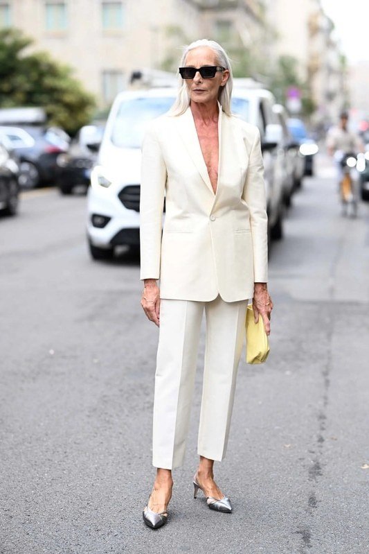 Woman over 50 wearing a cream suit with bright yellow clutch and silver heels