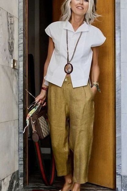Woman over 50 in a white top with mustard wide-leg trousers and pendant necklace