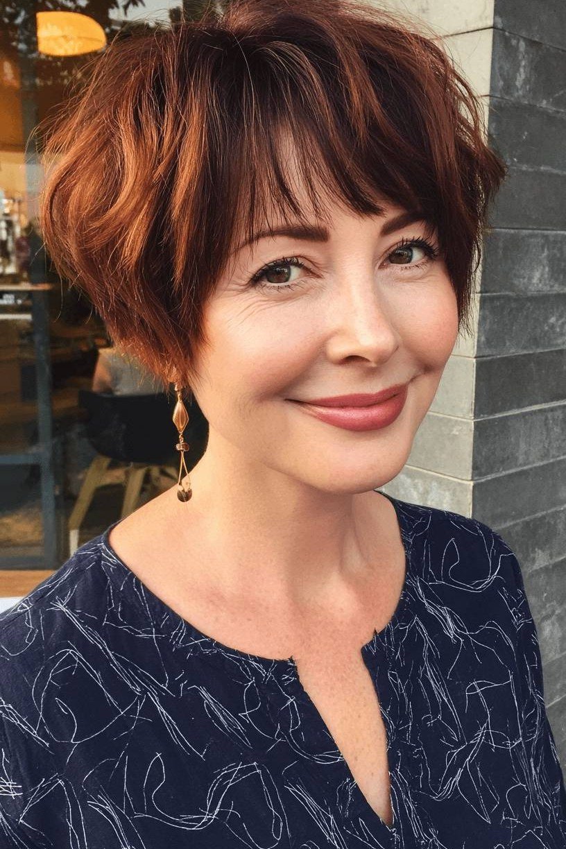Mature woman with a rich auburn short bixie haircut and full fringe.