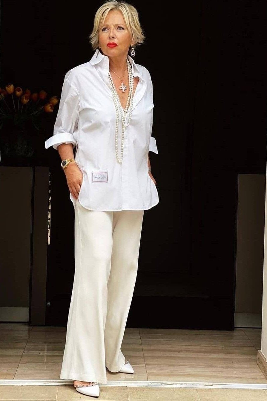 Woman over 50 wearing an oversized white shirt with white wide-leg trousers