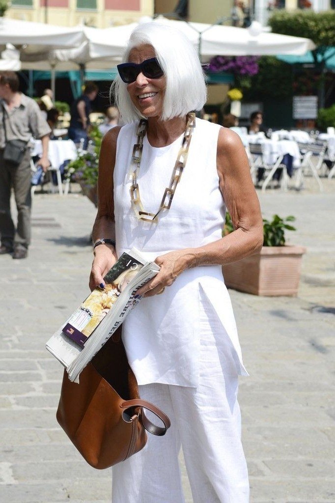 Woman over 50 wearing a white tunic with white cropped trousers and tan tote