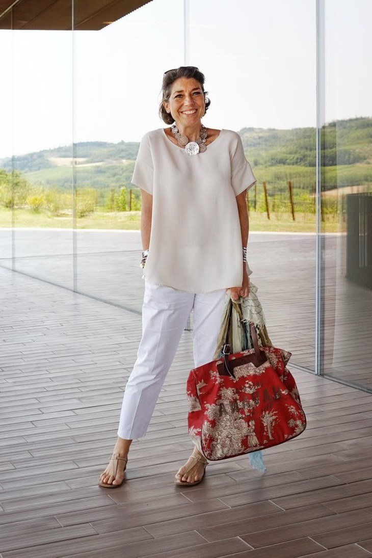 Woman over 50 in a cream t-shirt with white cropped trousers and red floral tote