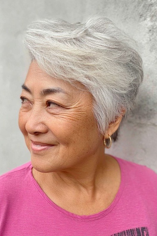 Older woman smiling with a feathered silver pixie haircut.